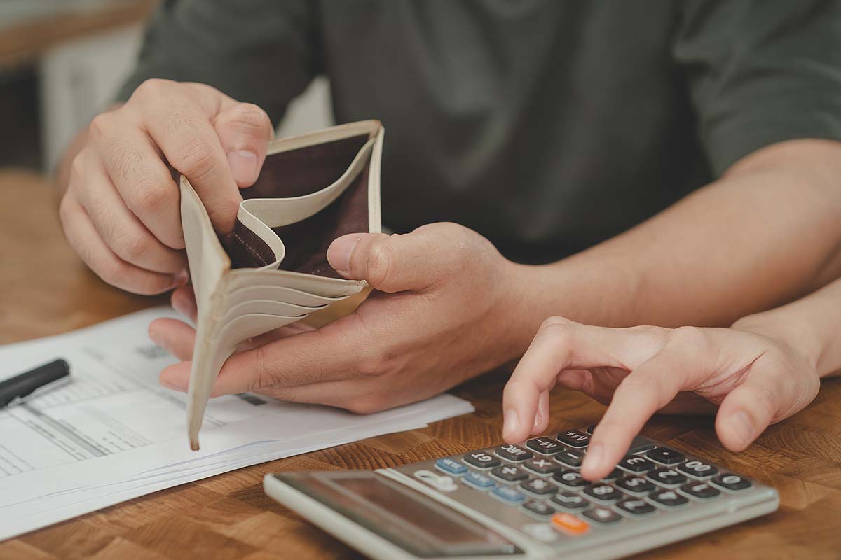 Person holding their empty wallet open while another person does financial calculations on a calculator
