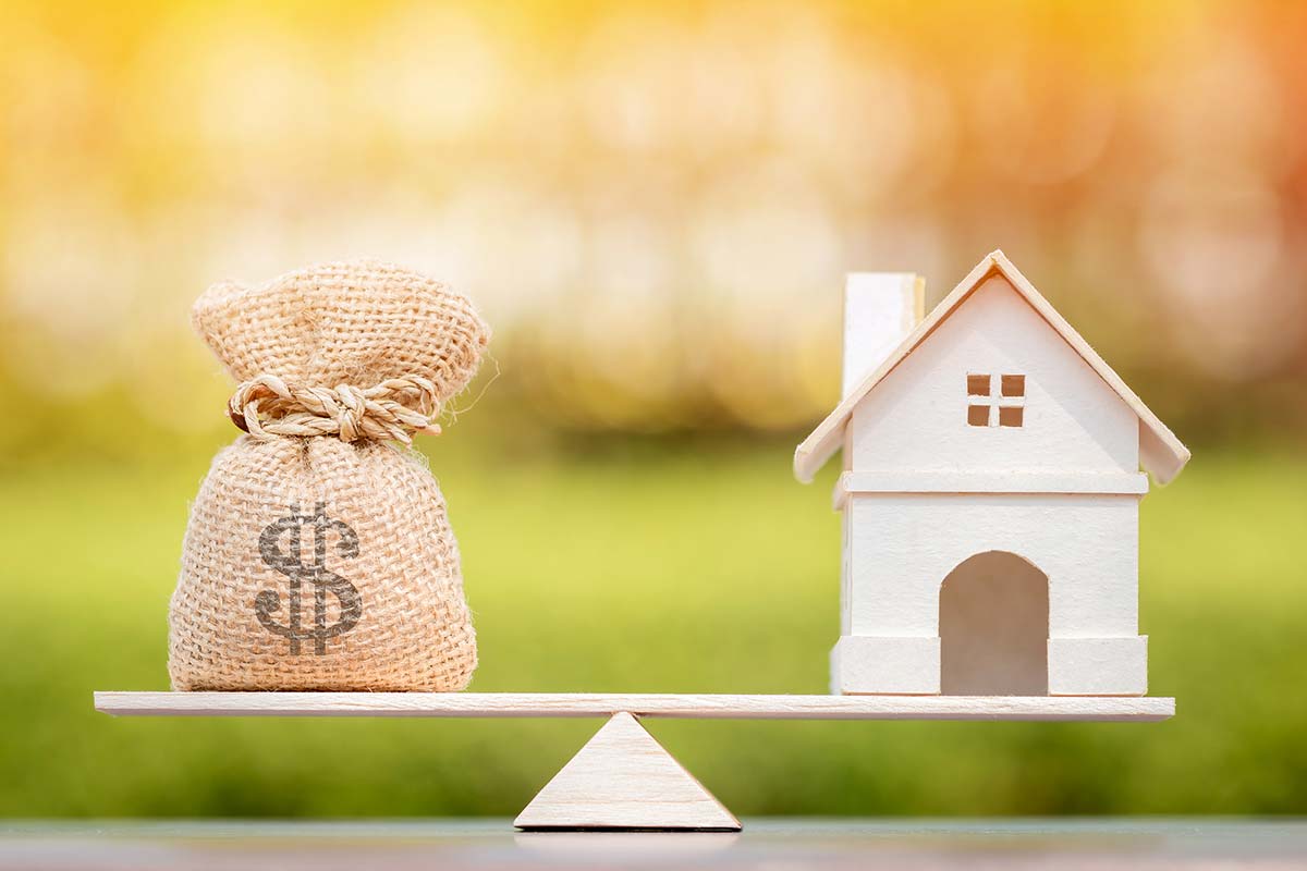A seesaw representing balance with a bag of money on one side and a house on the other