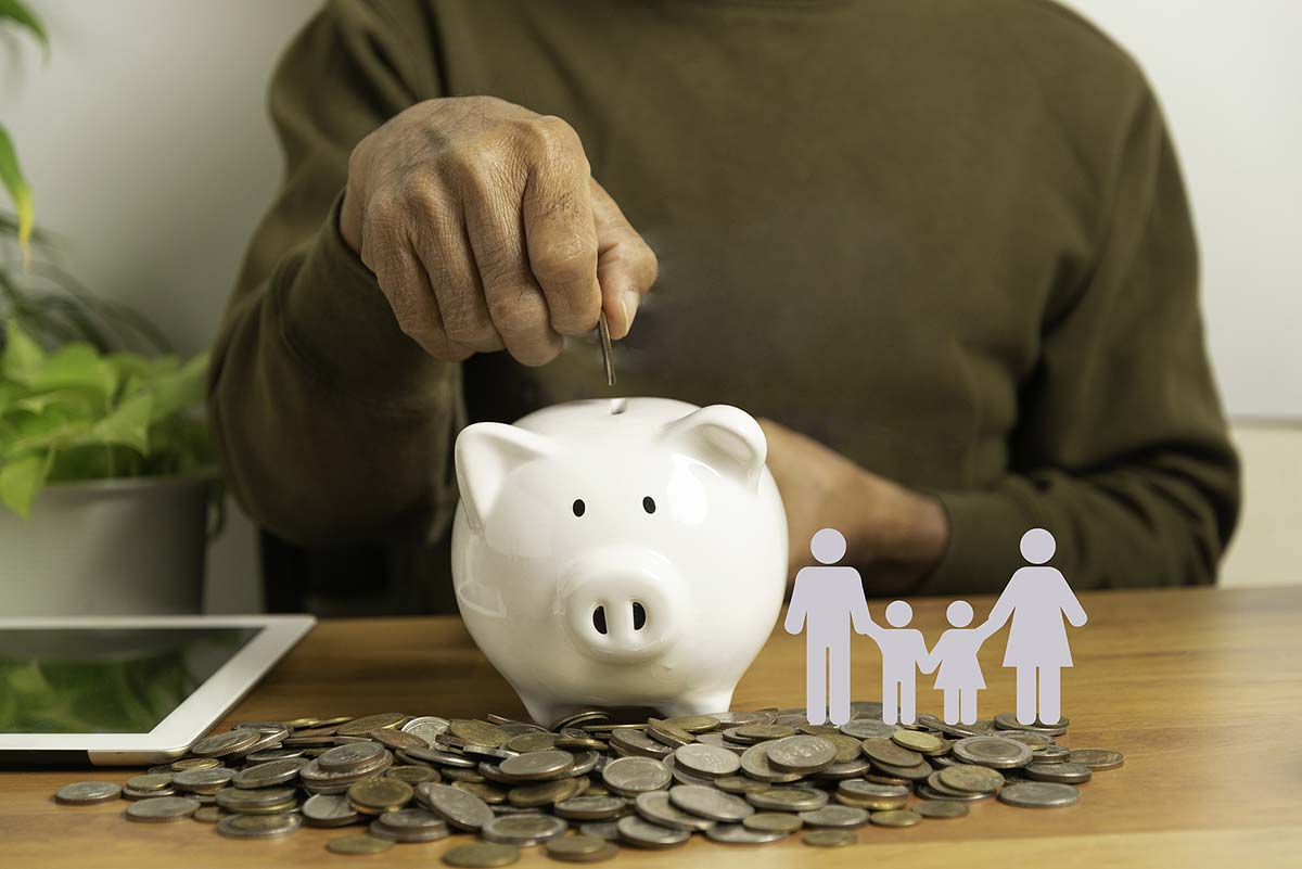 A person putting money into a piggy bank, with a paper cutout of a family next to it